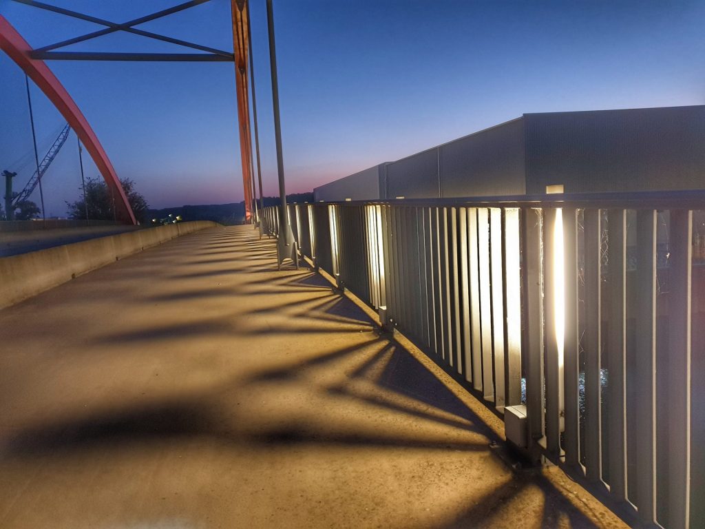 Bild von Licht und Schatten auf einer Brücke, wo das geländer beleuchtet ist. 