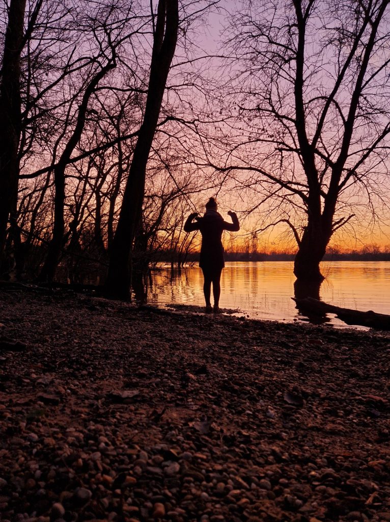 Powerpose am Wasser mit Sonnenuntergang im Hintergrund